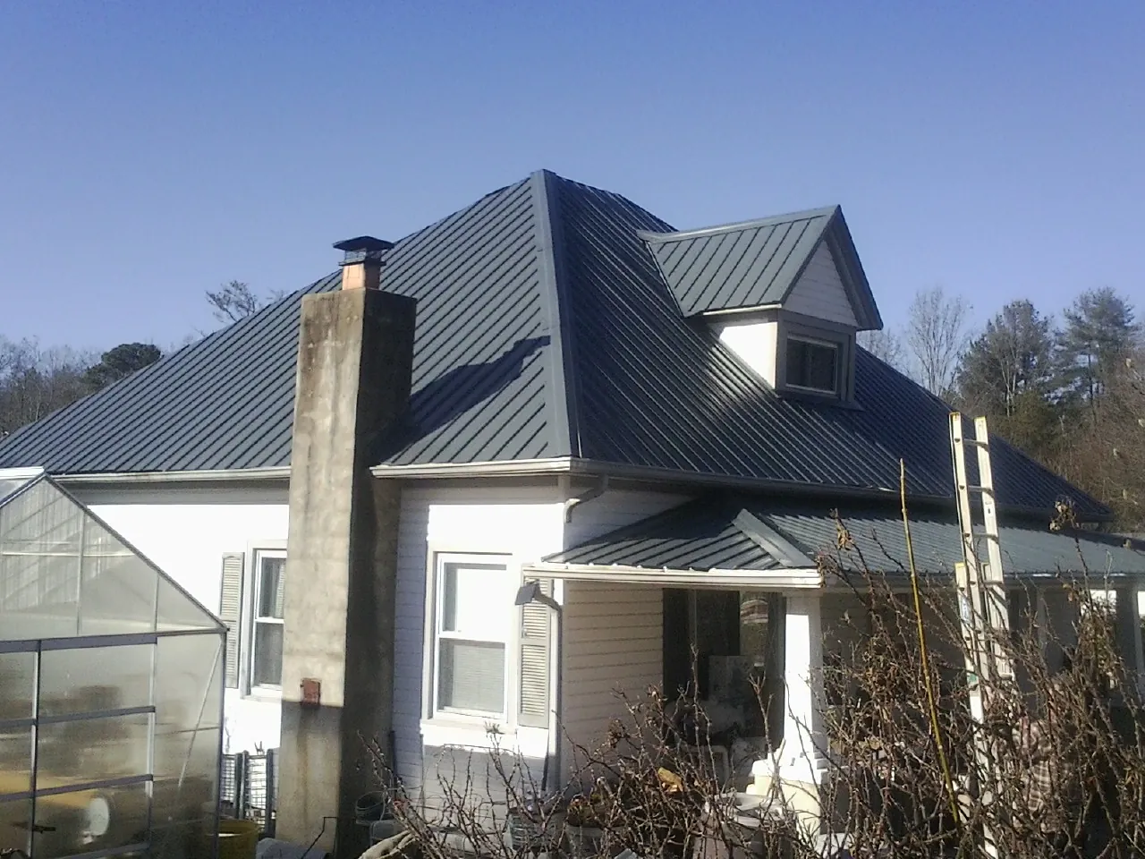 Dark blue standing seam metal roof on a white farmhouse with dormer — Slate & Tile Roof Repair by Roofing Brothers in Bearcreek