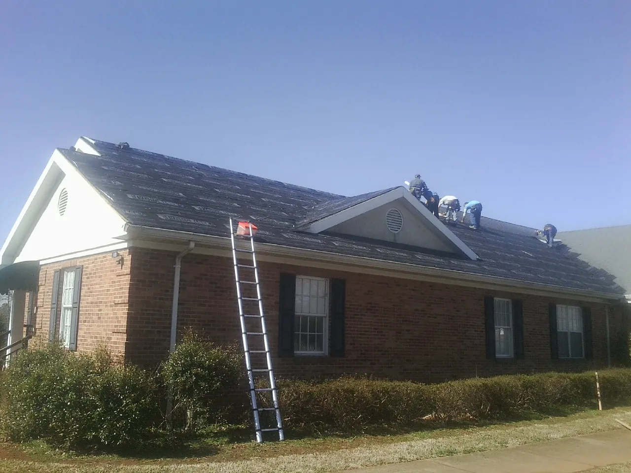 Crew tearing shingles off a brick ranch roof with a ladder set — Emergency Roof Repair work by our crew in Bearcreek