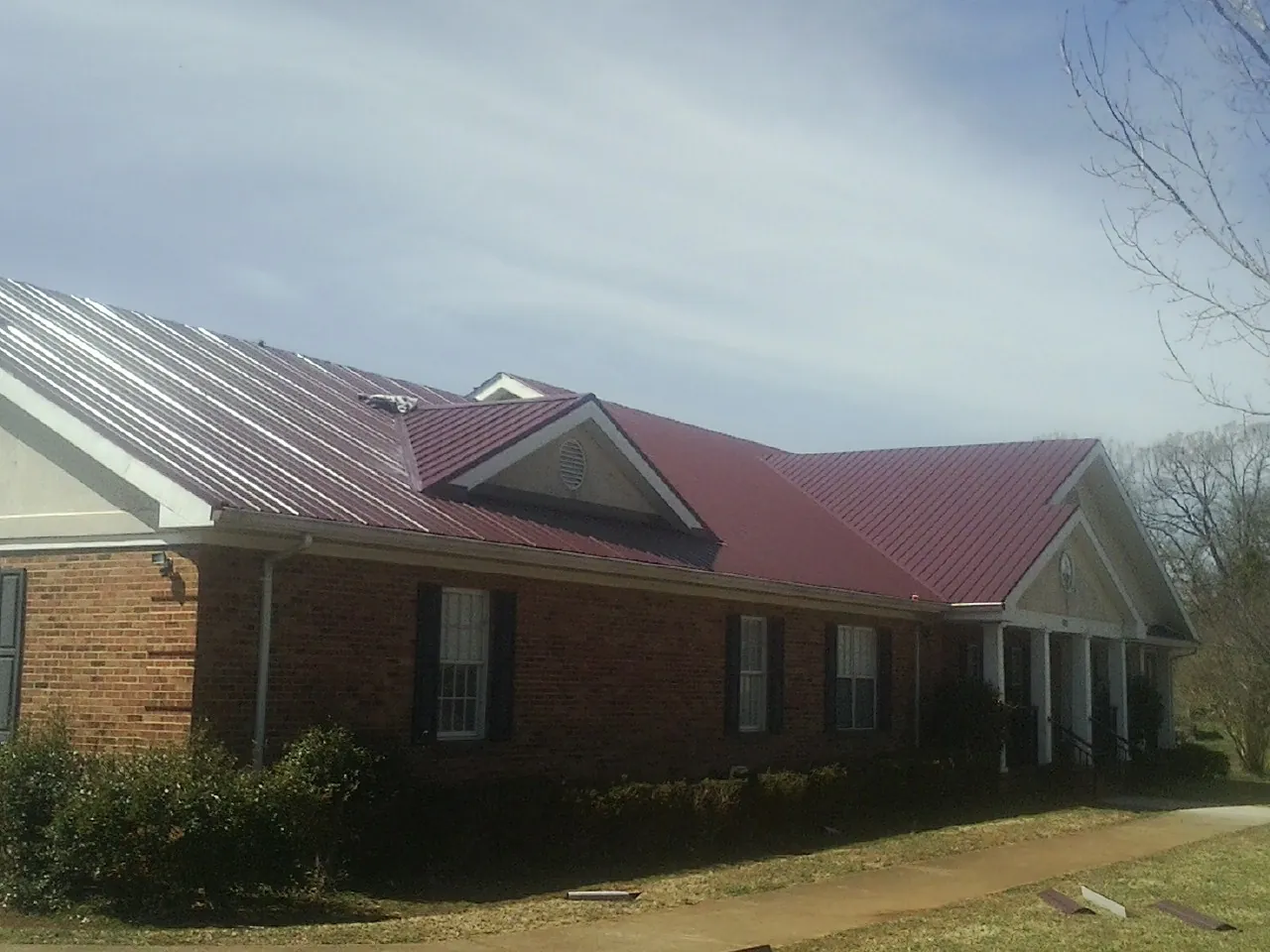 Red metal roof with gabled entries on a long brick building, from a Hail Damage Roof Repair job in Bearcreek