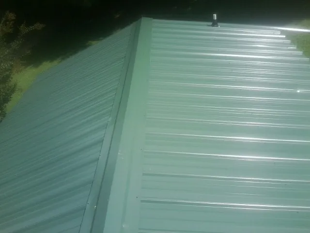 New green metal panels meeting at the ridge of a roof — Flat Roof Repair work by our crew in Bearcreek