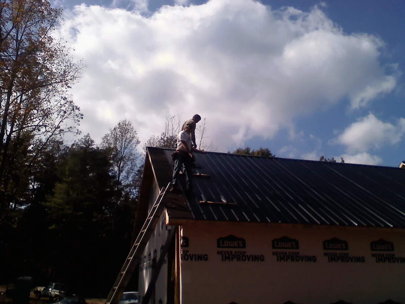 Roofer fastening dark metal panels high against a cloudy sky, from a Roof Inspection job in Bearcreek