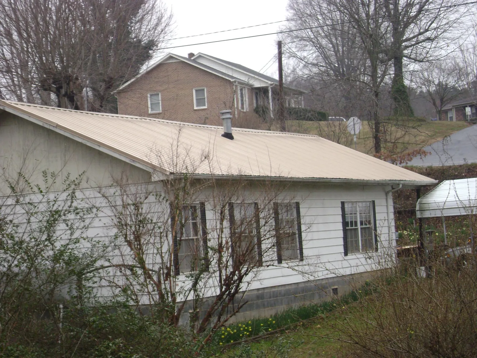 Tan metal roof on a white sided house set into a hillside — Commercial Roofing by Roofing Brothers in Bearcreek