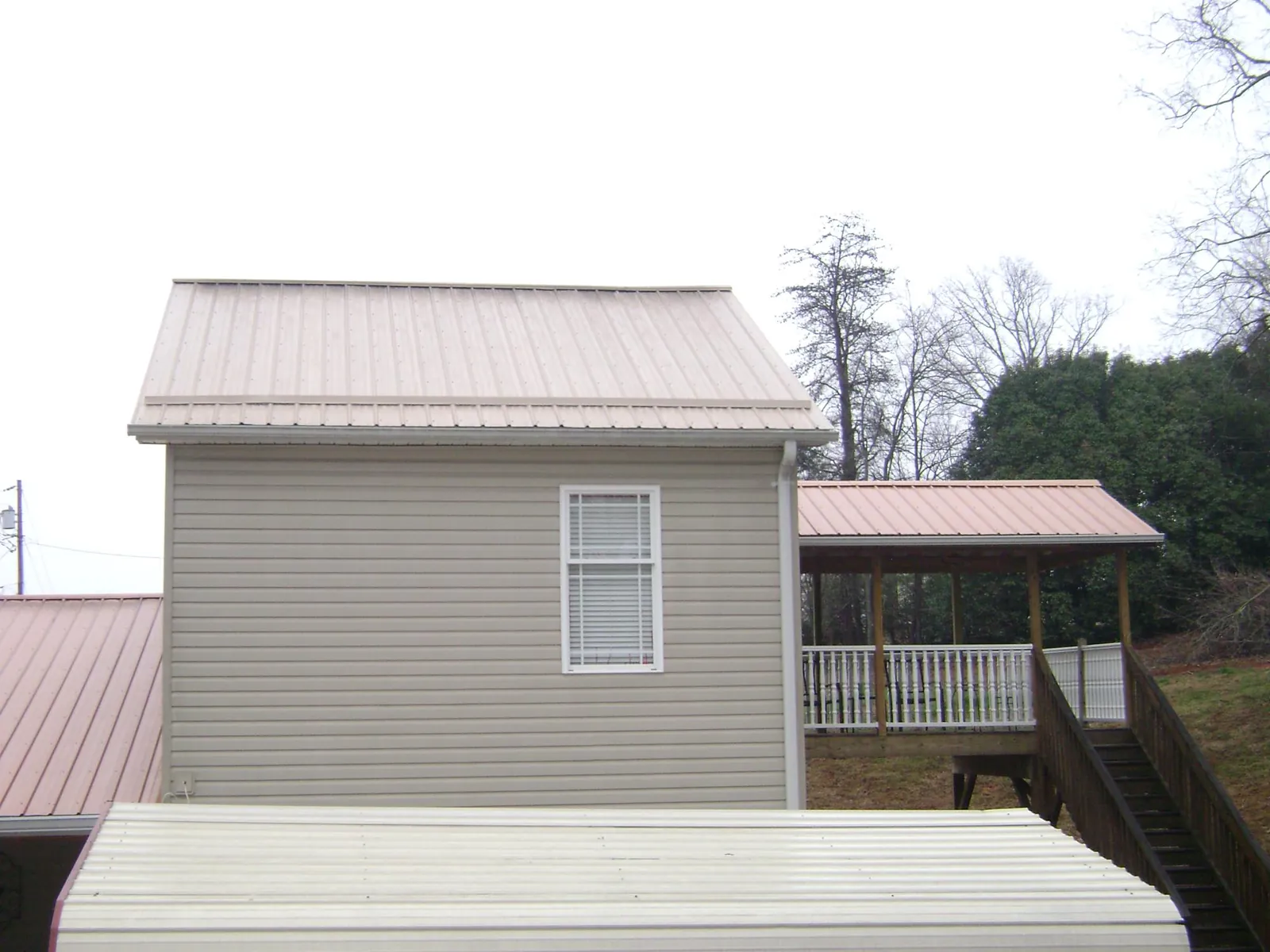 Tan metal roofs on a two story addition and attached porch, from a Roof Replacement job in Bearcreek